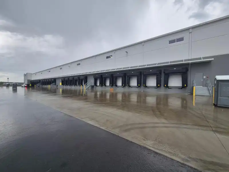 Large industrial warehouse with multiple loading dock doors and a wet concrete loading area.