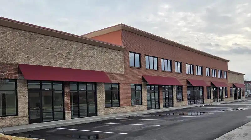 Two-story brick commercial building with red awnings, large windows, and an empty parking lot.