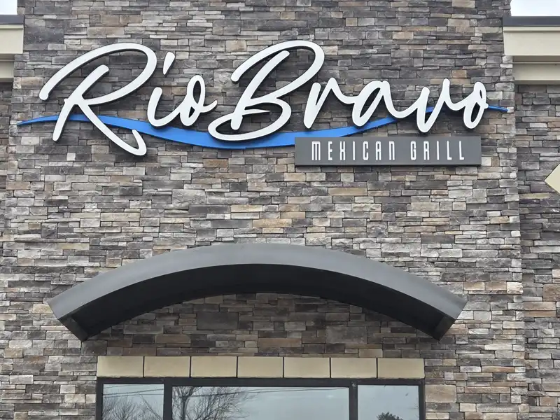 Curved metal entrance canopy mounted below the Rio Bravo Mexican Grill sign on a stone‑faced commercial building.