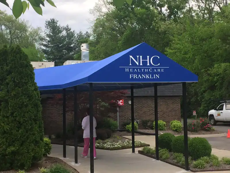 Covered walkway entrance to NHC Healthcare Franklin with a blue canopy and landscaped surroundings.