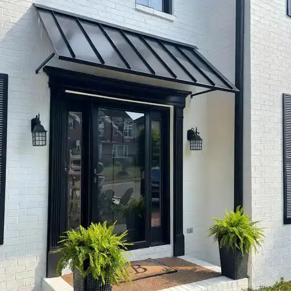 Black standing seam metal awning above a residential front door on a white brick house.