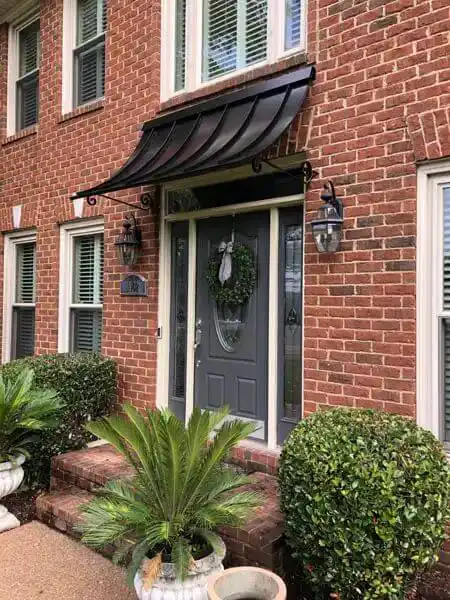 Concave metal door awning with decorative scroll brackets over a brick residential entry.