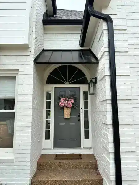 Standing seam metal awning above a residential front entry with arched doorway detail.