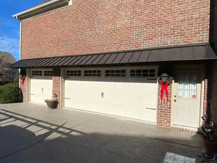Standing seam metal awning installed above multiple garage doors on a brick residential home.