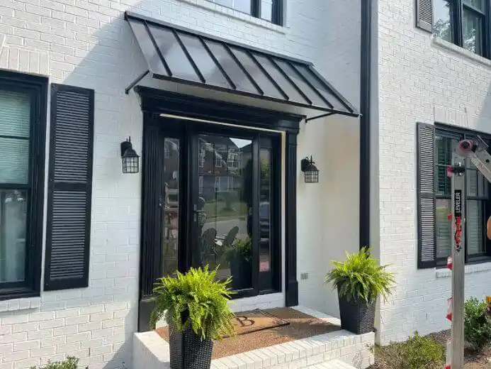 Black standing seam metal awning above a residential front door on a white brick house.
