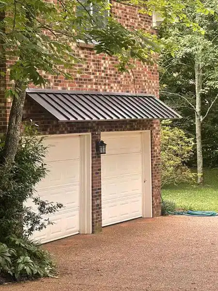 Metal garage awning spanning above double garage doors on a brick home exterior.