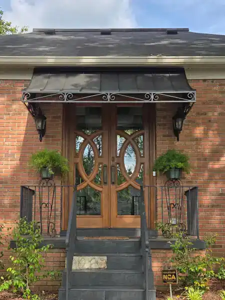 Metal door awning with scroll brackets installed over a residential entryway.