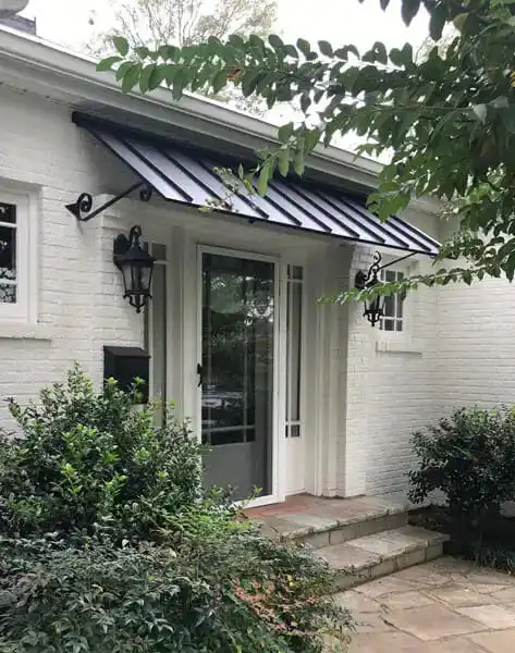 Straight metal door awning with decorative scroll brackets above double wood entry doors.
